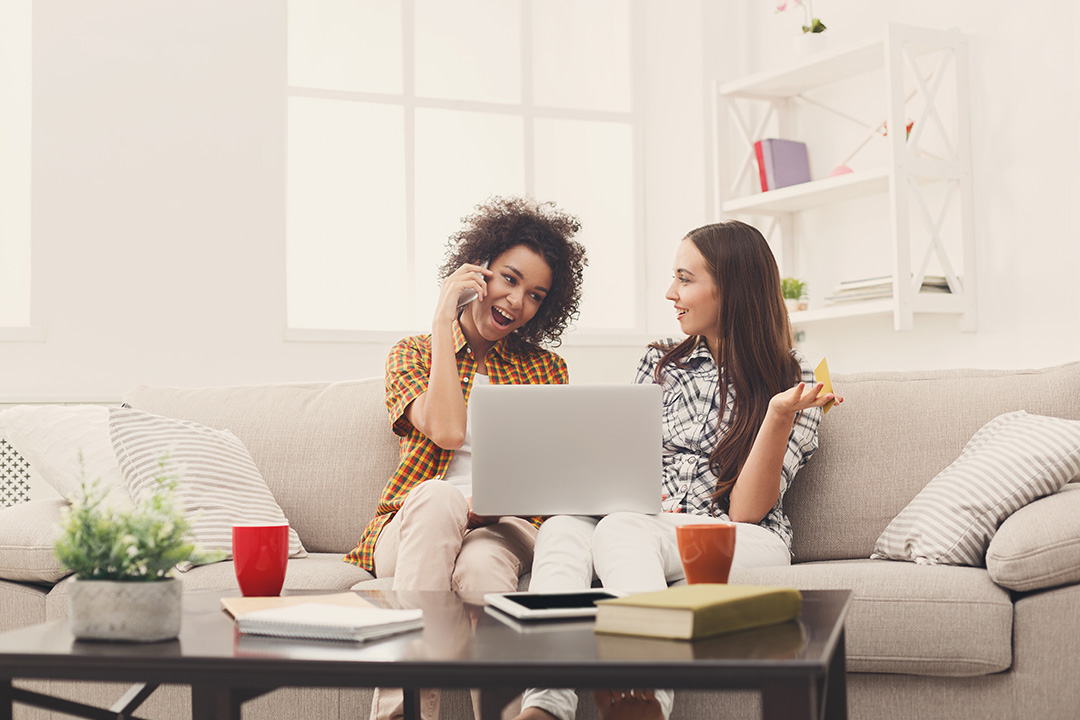 Two girls sitting on sofa with laptop